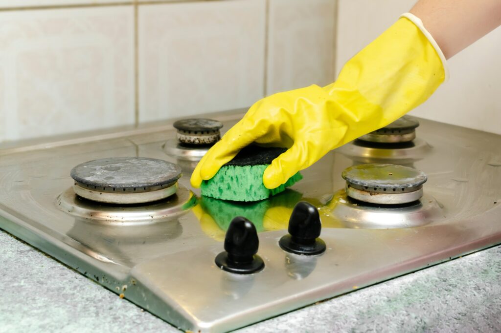 Cleaning dirty gas stove from grease, food leftovers.hand sponge detergent washing kitchen stove