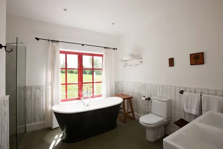 Pristine bathroom featuring a bathtub and sink, with red-framed French doors in the background, showcasing a spotless result after cleaning commonly neglected areas.