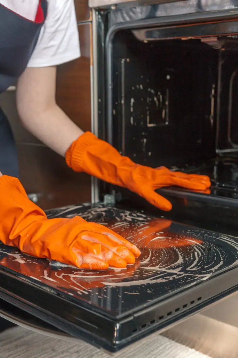End Of Lease Oven Cleaning In Two Rocks 4 Orange-gloved hands apply thick white chemical foam to the oven door and interior surface, performing a deep clean during bond cleaning before a rental property handover.