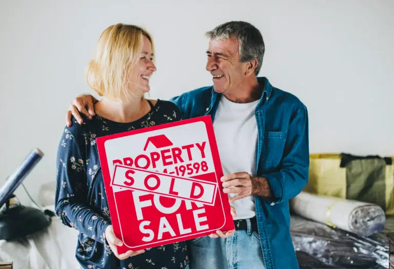 A happy couple stands next to a “For Sale” sign marked “Sold” in front of their house, celebrating the sale and high return on investment after using professional pre-sale cleaning services in Perth